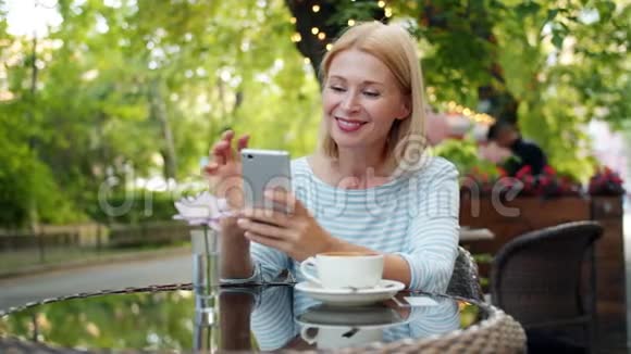 在外面的咖啡馆里快乐的女人用智能手机触摸屏幕的缓慢动作视频的预览图