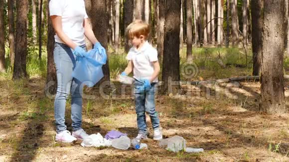一个小男孩在树林里收集垃圾和他的母亲一起放进一个袋子里家庭活动家关心大自然视频的预览图