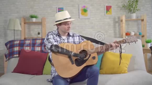 戴着仿生假臂的帽子的年轻人坐在沙发上弹吉他视频的预览图