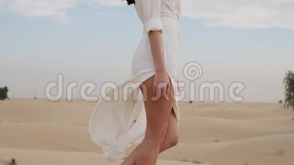 一个光着脚穿着白色连衣裙的黑发女人沿着沙漠沙走慢动作视频的预览图