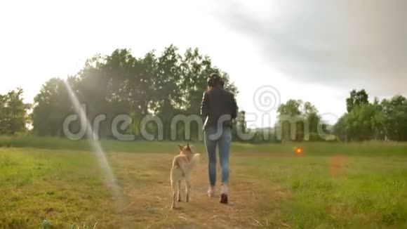 戴着耳机的漂亮女人和她的狗在公园里散步视频的预览图