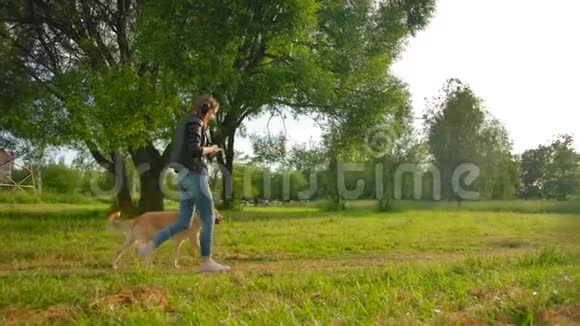 一个戴着耳机的女孩和她的狗在公园里散步的平行景色视频的预览图
