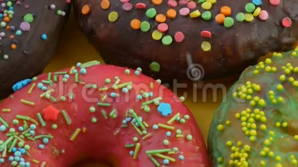 美国甜甜圈五颜六色的釉和粉末在黄色背景上旋转近距离观看视频的预览图