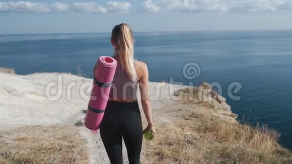 从侧面看穿着运动服的女士带着体操垫来到悬崖边视频的预览图