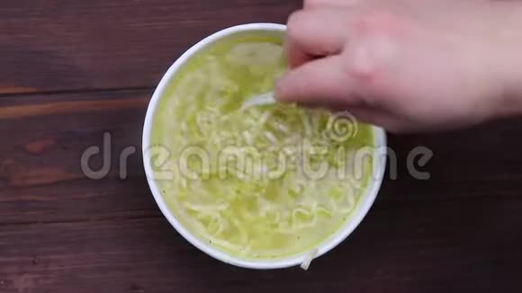 特写镜头一只手用白色塑料叉子搅动面条纸张的容量汤在煮视频的预览图