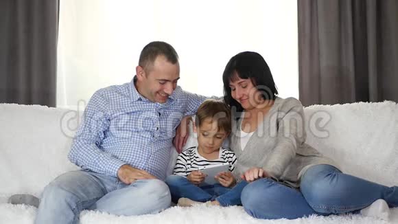 父亲母亲和儿子一起在平板电脑上看电影幸福家庭的概念视频的预览图