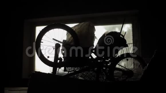旧自行车和其他旧东西收集在阁楼的房子的窗户背景黑暗的轮廓特写视频的预览图