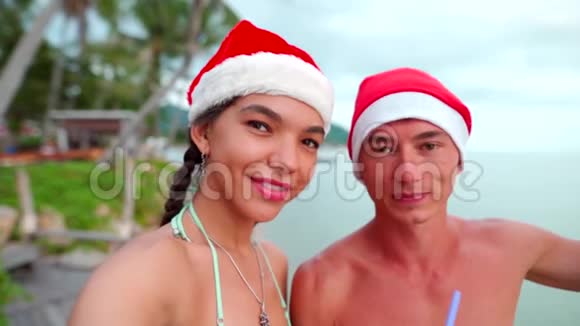 在海滩度假时戴着圣诞帽的自画像一对幸福的夫妇在镜头前微笑视频的预览图
