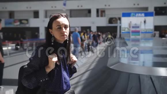 一位女士站在Ajroport的移动行李带附近正在等待她的手提箱视频的预览图