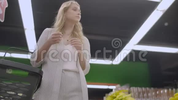 穿着休闲装的漂亮女士走在杂货店里手里拿着食物的购物车看上去很漂亮视频的预览图