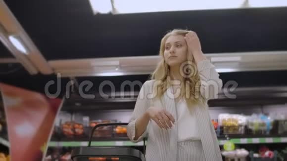 一个女买家在杂货店里拿着篮子走在货架和柜台之间看着商品和产品视频的预览图