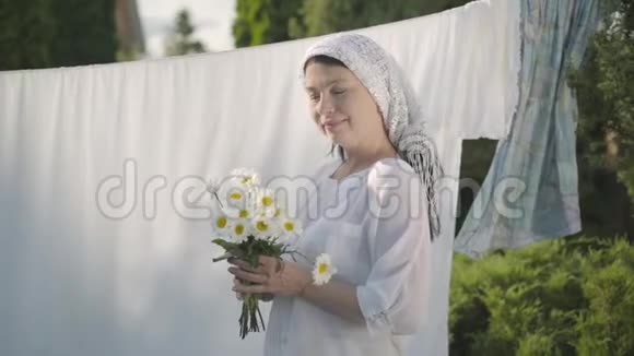 可爱的成熟女人头上戴着白色披肩在户外的晾衣绳上撕下雏菊花瓣华盛顿积极正面视频的预览图