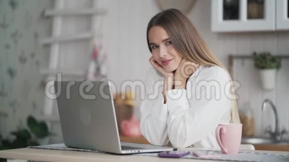 年轻漂亮的女人在家里做笔记本电脑看着相机微笑视频的预览图