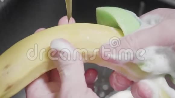 人用洗涤供应商和海绵清洗香蕉泡沫在手上和香蕉上黑色水槽在背景上关门视频的预览图
