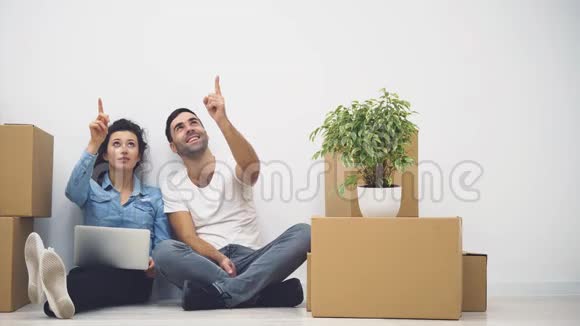 年轻夫妇正一起搬到一间新公寓他们在看着并指向女人拿着笔记本电脑4K视频的预览图