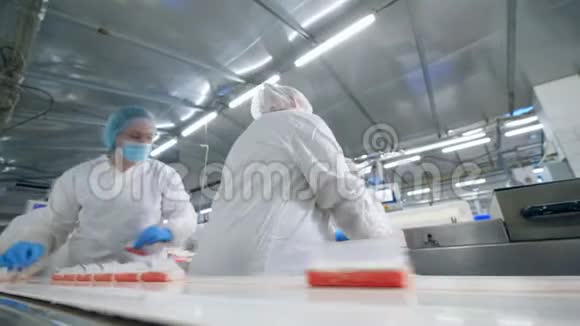 女专家正在把鱼零食从传送带上移开工厂工人穿着防护服包装食品视频的预览图