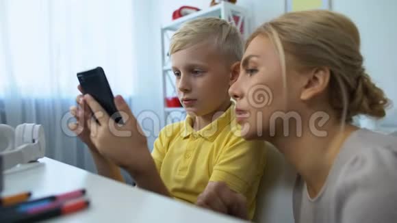 可爱的男孩向妈妈展示新的智能手机应用程序现代技术小玩意视频的预览图