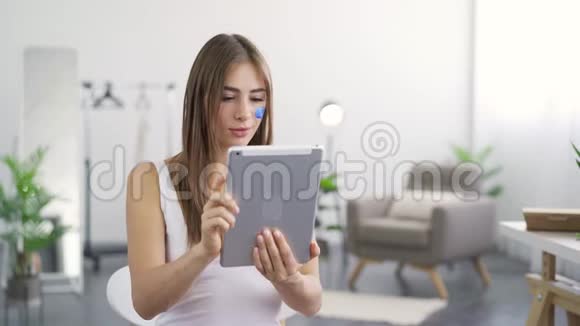 年轻可爱的女人坐在家里的平板电脑上得到好消息的肖像女孩脸上画的留言框视频的预览图