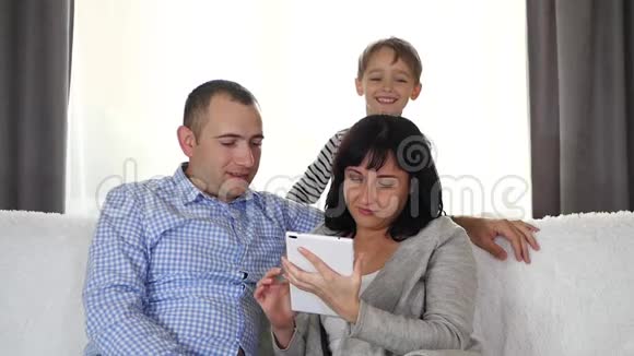 妈妈爸爸和宝宝在一起一男一女坐在沙发上用平板电脑小男孩躲起来视频的预览图