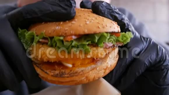 戴着黑色橡胶手套的少年正在吃汉堡美味多汁的新鲜汉堡摆在桌上的快餐视频的预览图