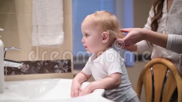妈妈在浴室镜子前梳着她小女儿的头发视频的预览图