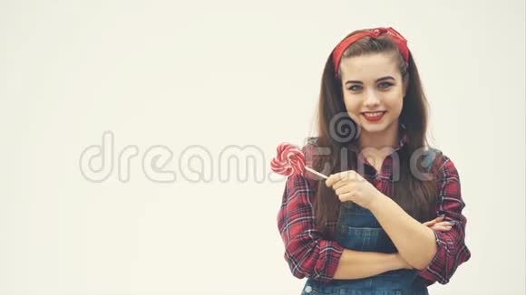 可爱迷人的女孩站在红色的心形棒棒糖微笑和摆姿势视频的预览图