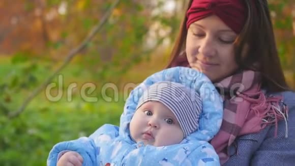 年轻快乐的母亲在秋天的公园里抱着一个胖乎乎的婴儿亲吻脸颊产妇概念视频的预览图