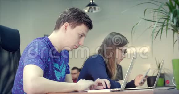 年轻人在办公室使用电脑和手机两位设计师同事一起工作视频的预览图