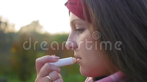 迷人的年轻女子把她的嘴唇涂在绿色森林的背景上女孩画她的嘴唇近距离射击视频的预览图
