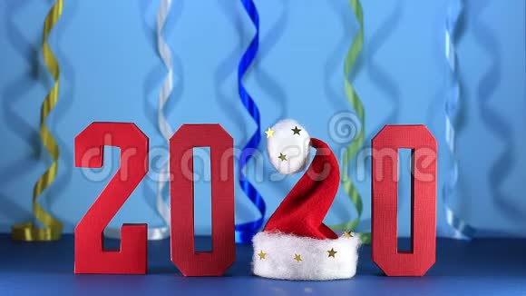 红色几何数字2020和下降纸屑在蓝色背景与彩色蛇纹石表格2中的圣诞老人帽子视频的预览图
