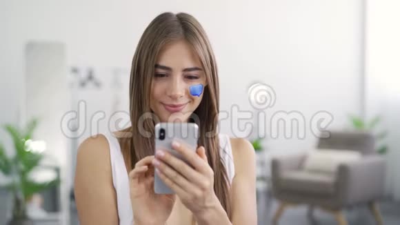 年轻可爱的女人坐在家里用手机微笑的肖像女孩脸上画的留言框视频的预览图