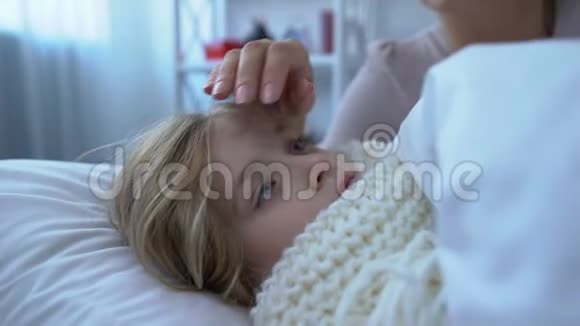 爱抚的妈妈摸着额头裹着围巾躺在床上的小女儿视频的预览图