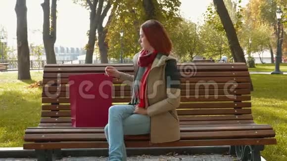 一个长着狐臭头发的女孩坐在长凳上从一个红色的纸袋里拿出药片开始使用它视频的预览图