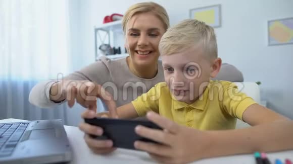 妈妈和小儿子一起玩智能手机休闲时间和应用程序的新游戏视频的预览图