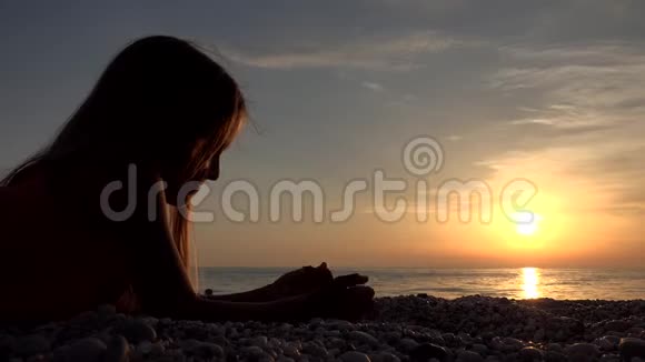 海滩上的孩子日落时在海滩上玩耍的孩子看着女孩在学习卵石视频的预览图