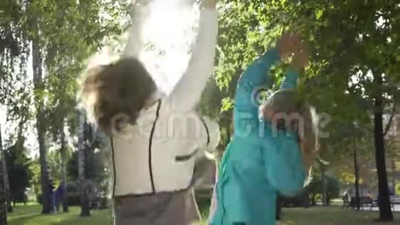 特写白种人的祖母和孙女在阳光下辗转树叶跳跃和旋转两个快乐视频的预览图