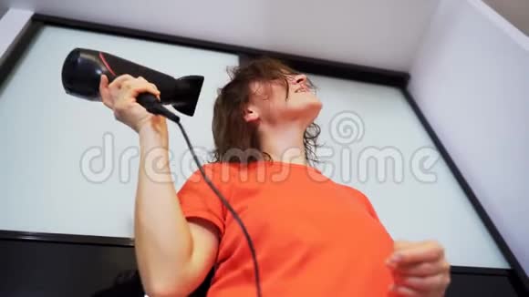 一个穿红色T恤的女人用吹风机擦干头发视频的预览图