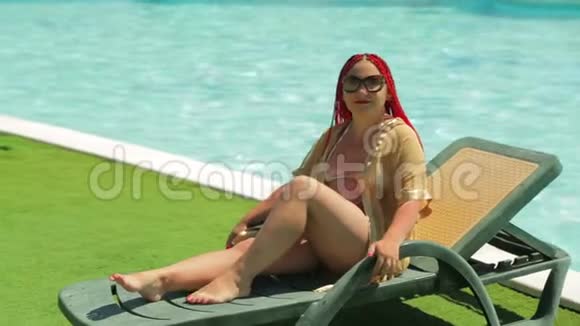 一个年轻的黑发女人正在游泳池附近的一张躺椅上晒太阳视频的预览图