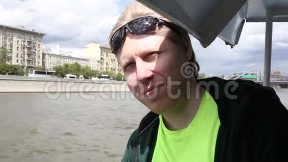 太阳眼镜男青年的特写镜头眼睛对着水面眨着眼睛漂浮在莫斯科河的船只上视频的预览图