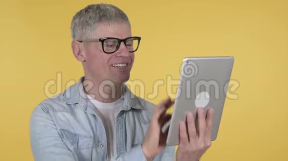 黄色背景下的临时老人通过平板进行视频聊天视频的预览图