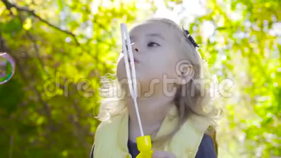 迷人的金发女孩呆在阳光下吹肥皂泡有棕色眼睛的小孩在公园里玩耍视频的预览图