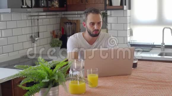 有魅力的帅哥留着胡子在厨房的笔记本电脑上看比赛视频的预览图