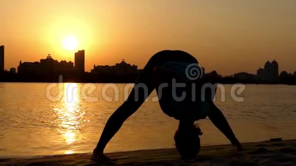 女孩练习瑜伽姿势宽缠向前弯曲日落时的行动视频的预览图