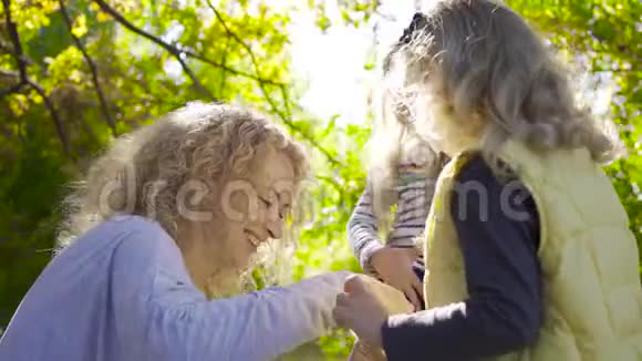 笑着一个留着卷发的白种人女人坐在阳光下和她漂亮的小女孩一起玩肥皂泡视频的预览图
