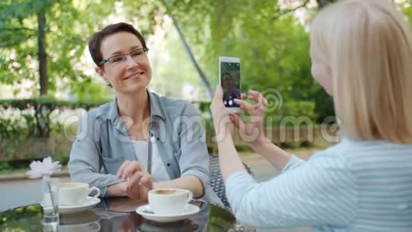 有魅力的女人在咖啡馆里摆着智能手机摄像头挥舞着手视频的预览图