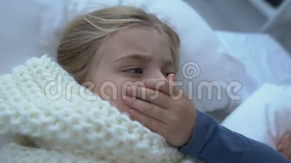 戴围巾的可爱的女孩子在床上咳嗽慈爱的母亲抚摸着孩子的额头视频的预览图