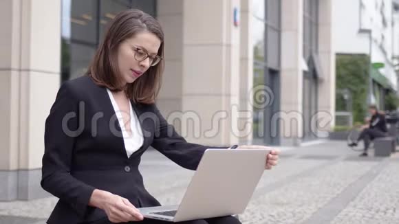 穿正装的女士在办公楼外使用笔记本电脑视频的预览图