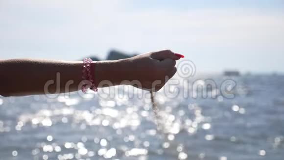 女人手里拿着一把沙子母臂浇黄色干沙抵御海景海面上闪耀着视频的预览图