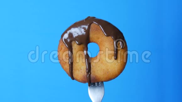 叉子上的一个大圆甜甜圈巧克力糖霜在蓝色背景上流动视频的预览图