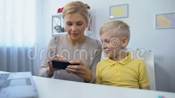 快乐的母亲和儿子一起在智能手机上玩游戏玩得开心APP视频的预览图